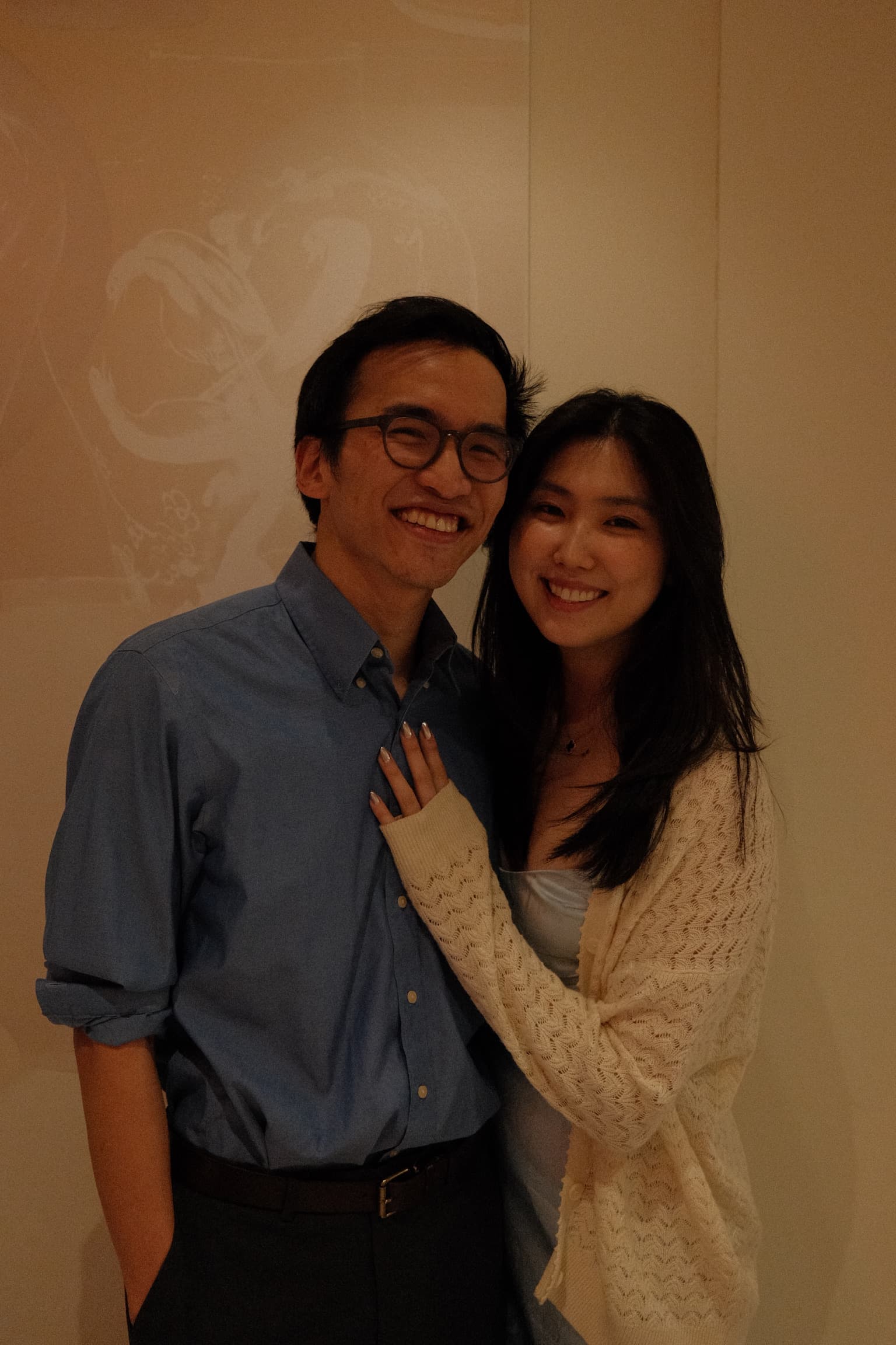 Arms around each other against a pale gallery wall.