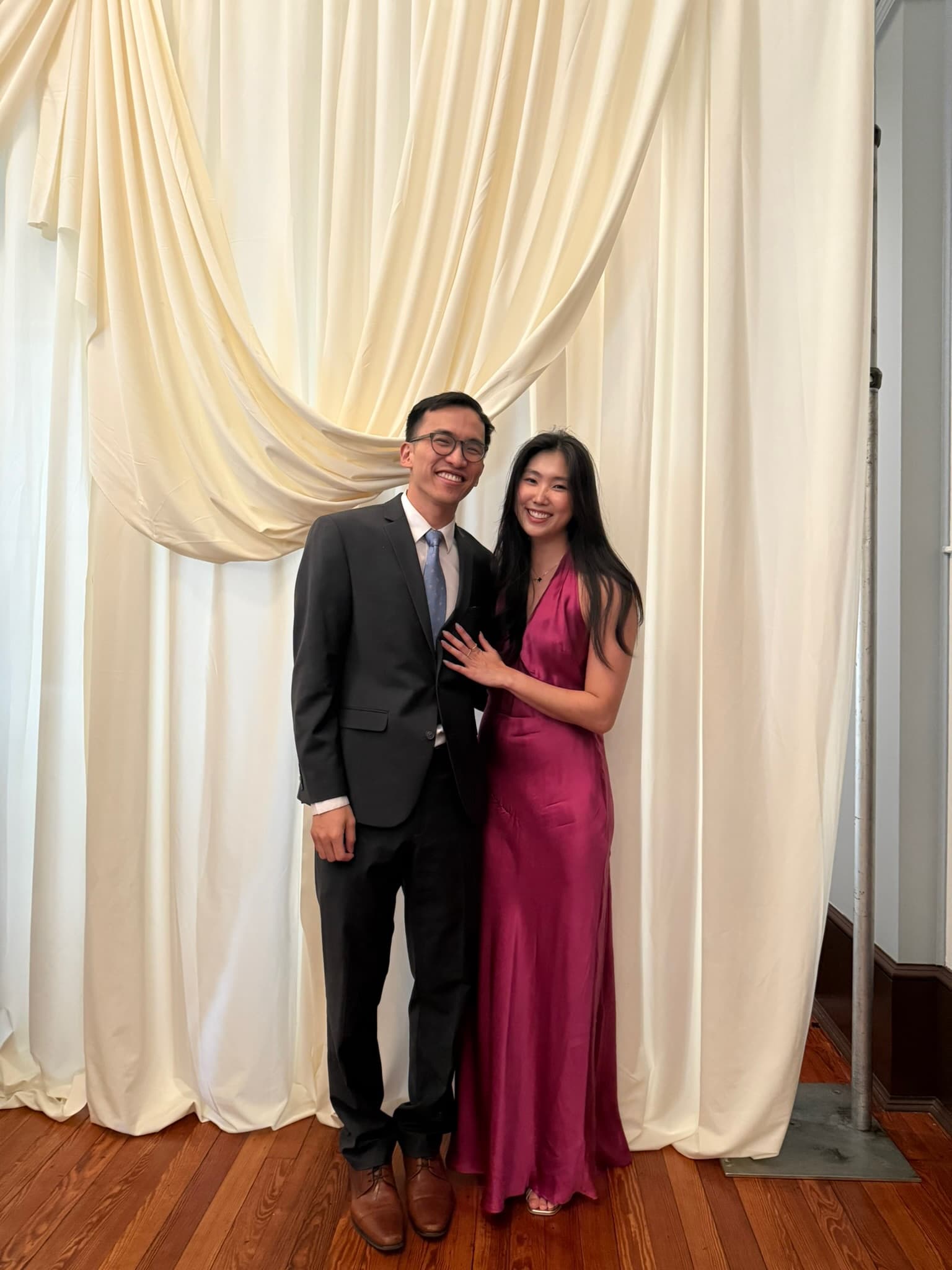 In a suit and a magenta gown, against a cream curtain.