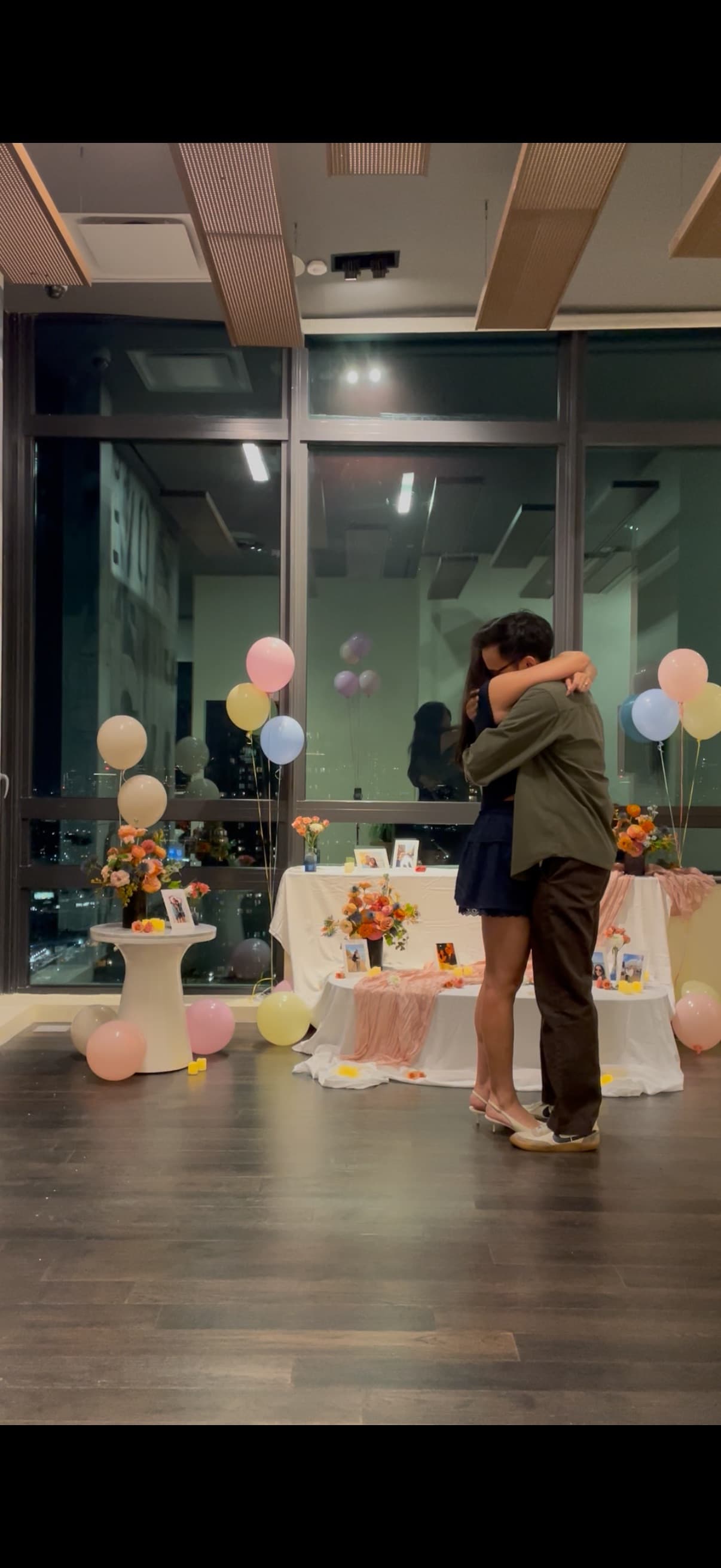 Mid-embrace in the room set up for the proposal, balloons and a decorated table around us.