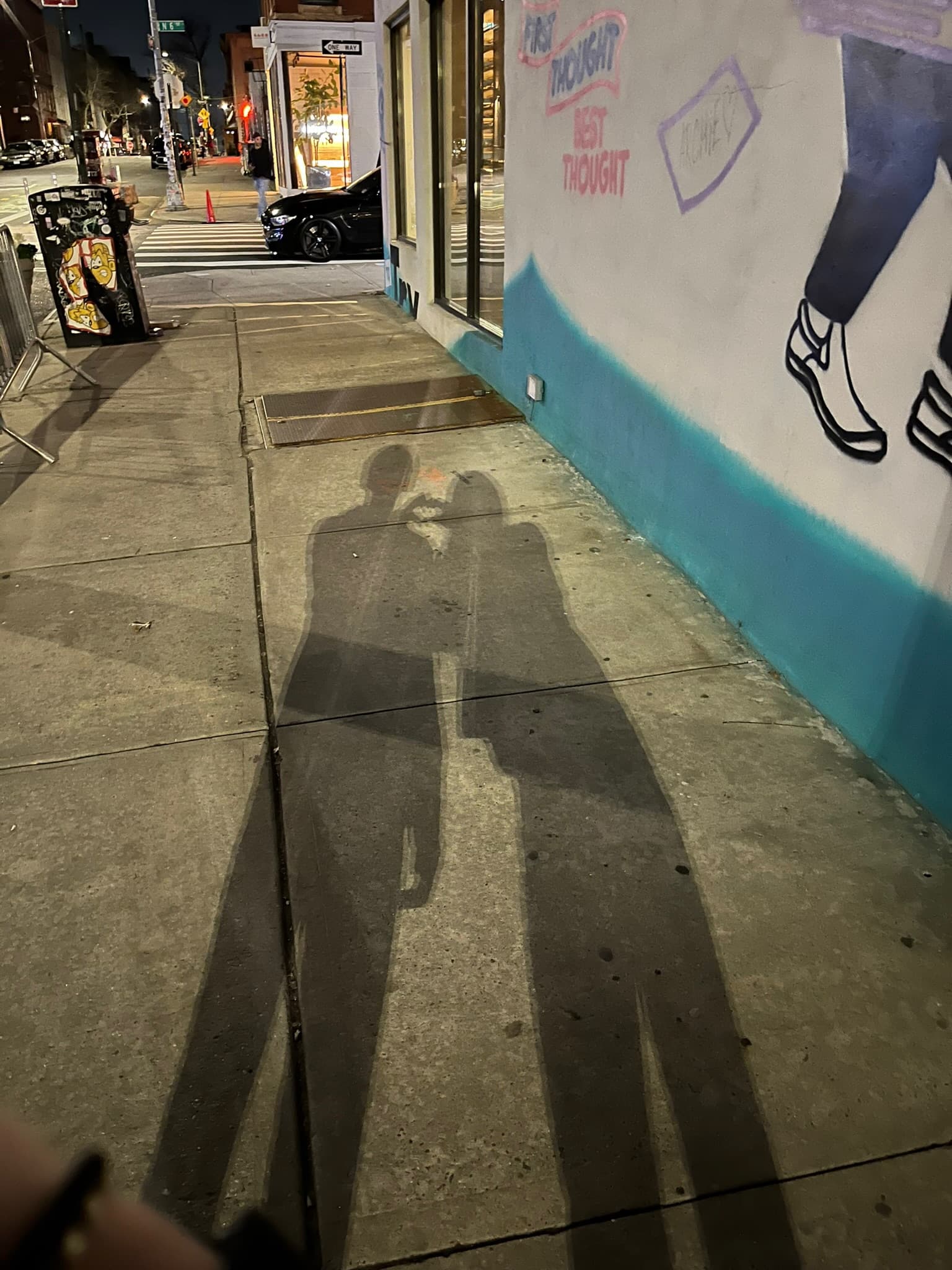 Our two shadows stretched down a sidewalk at night, beside a painted wall.