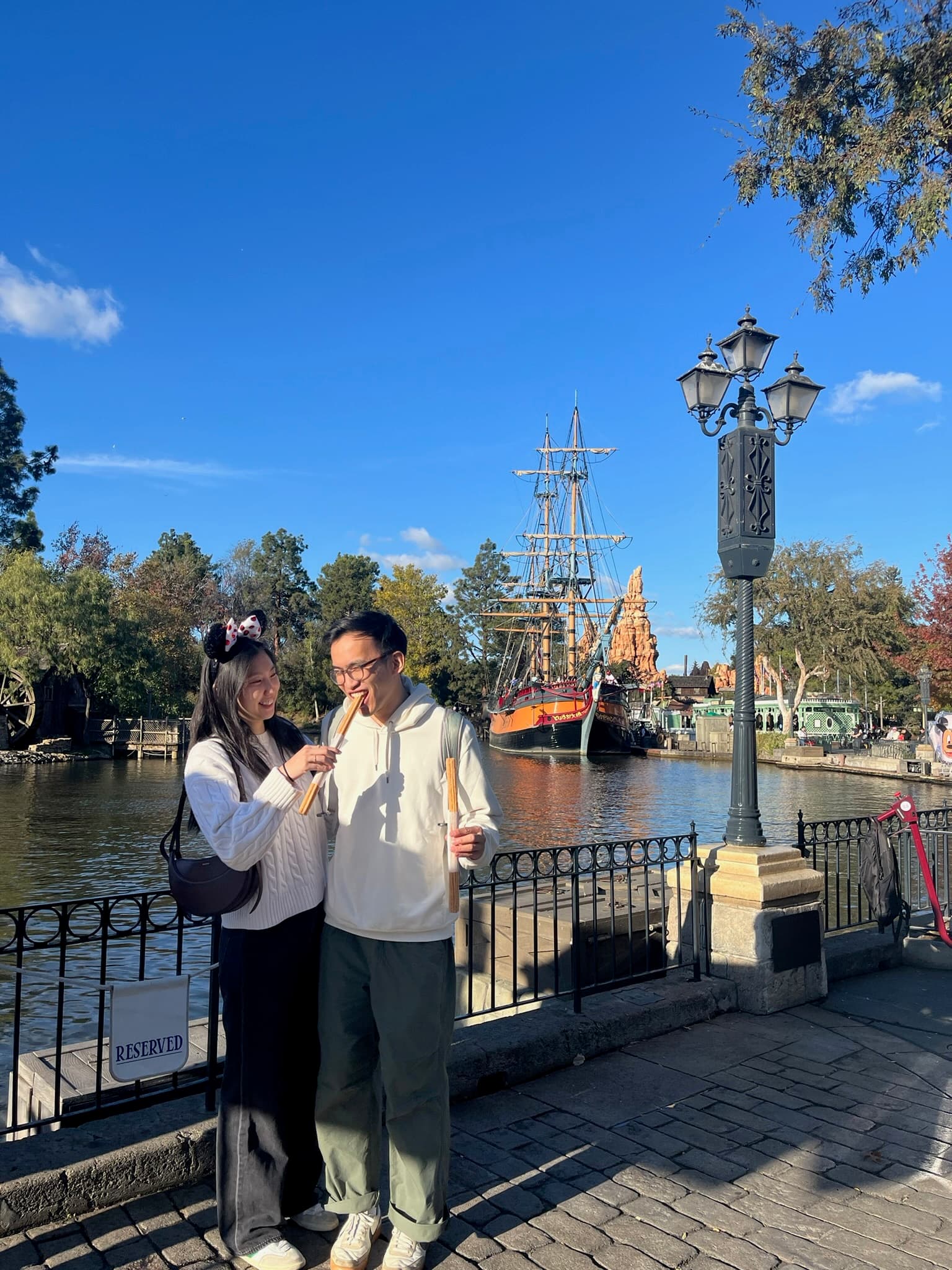 By the water at a theme park, a tall ship moored behind us.