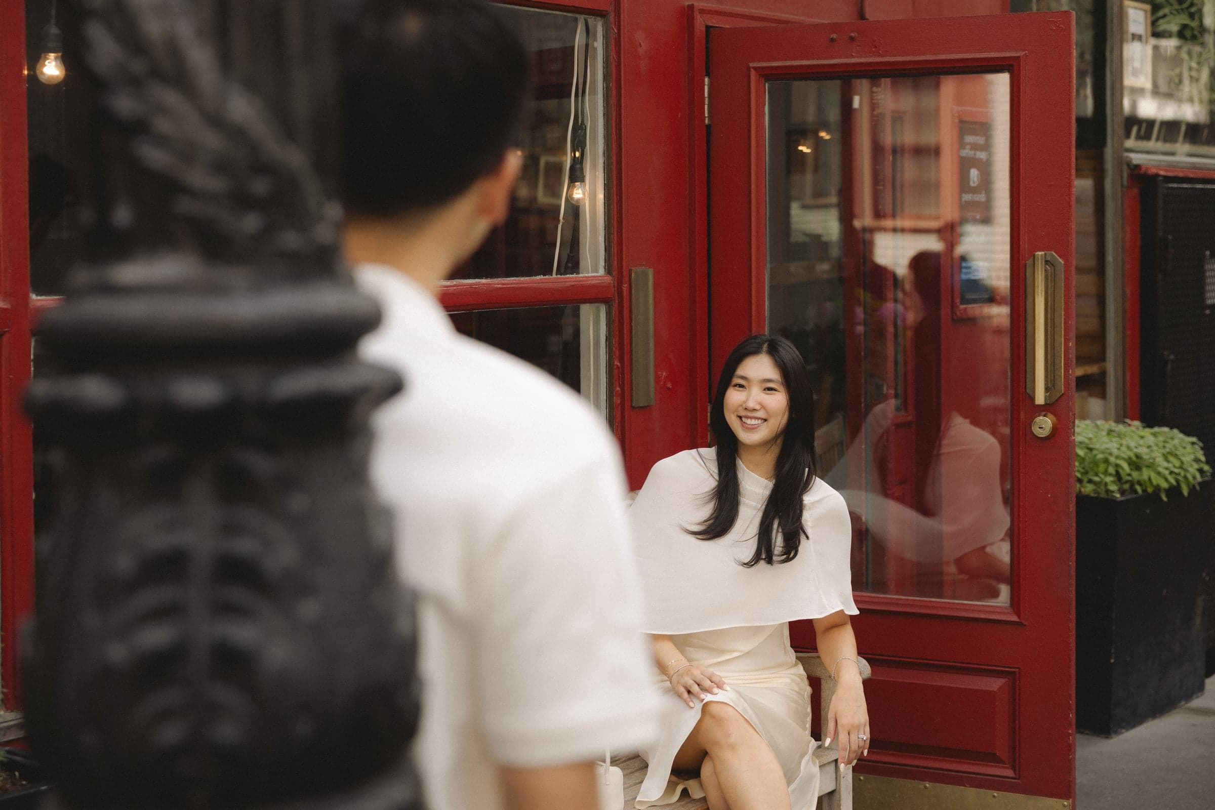 Sitting outside a bar with a bright red door, seen past the other's shoulder.
