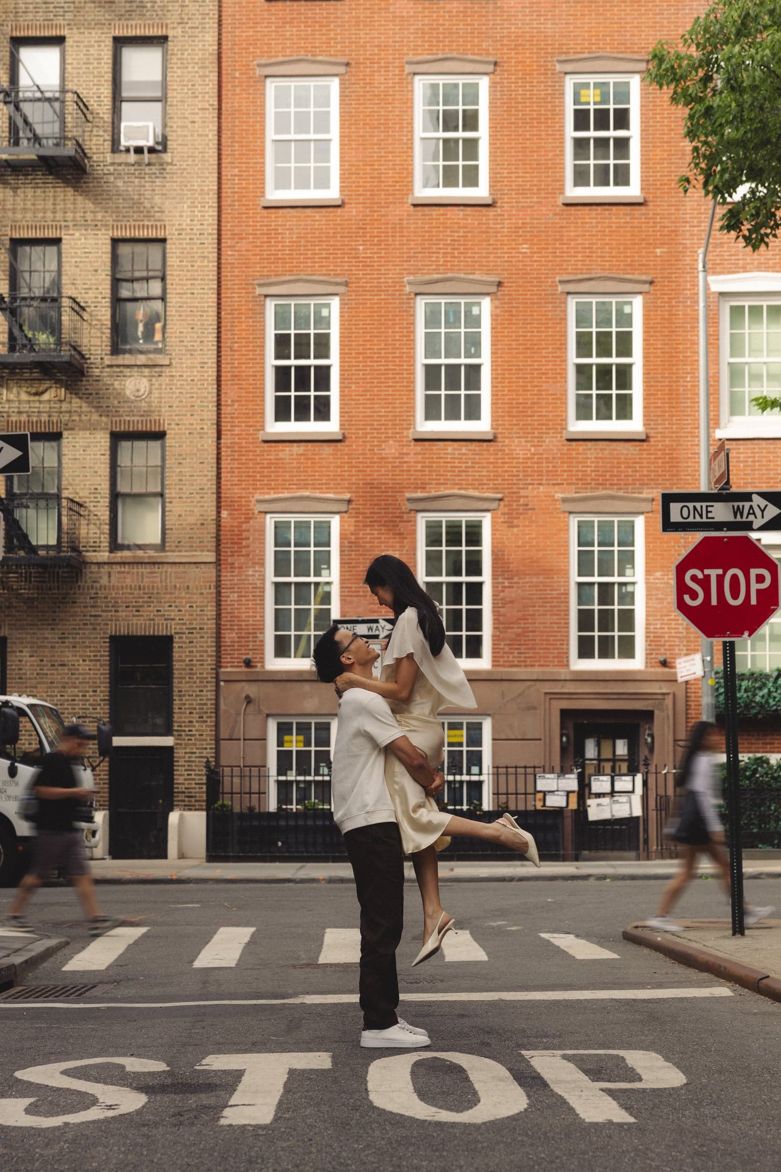 One of us lifting the other in the middle of a crosswalk, in front of a brick townhouse.