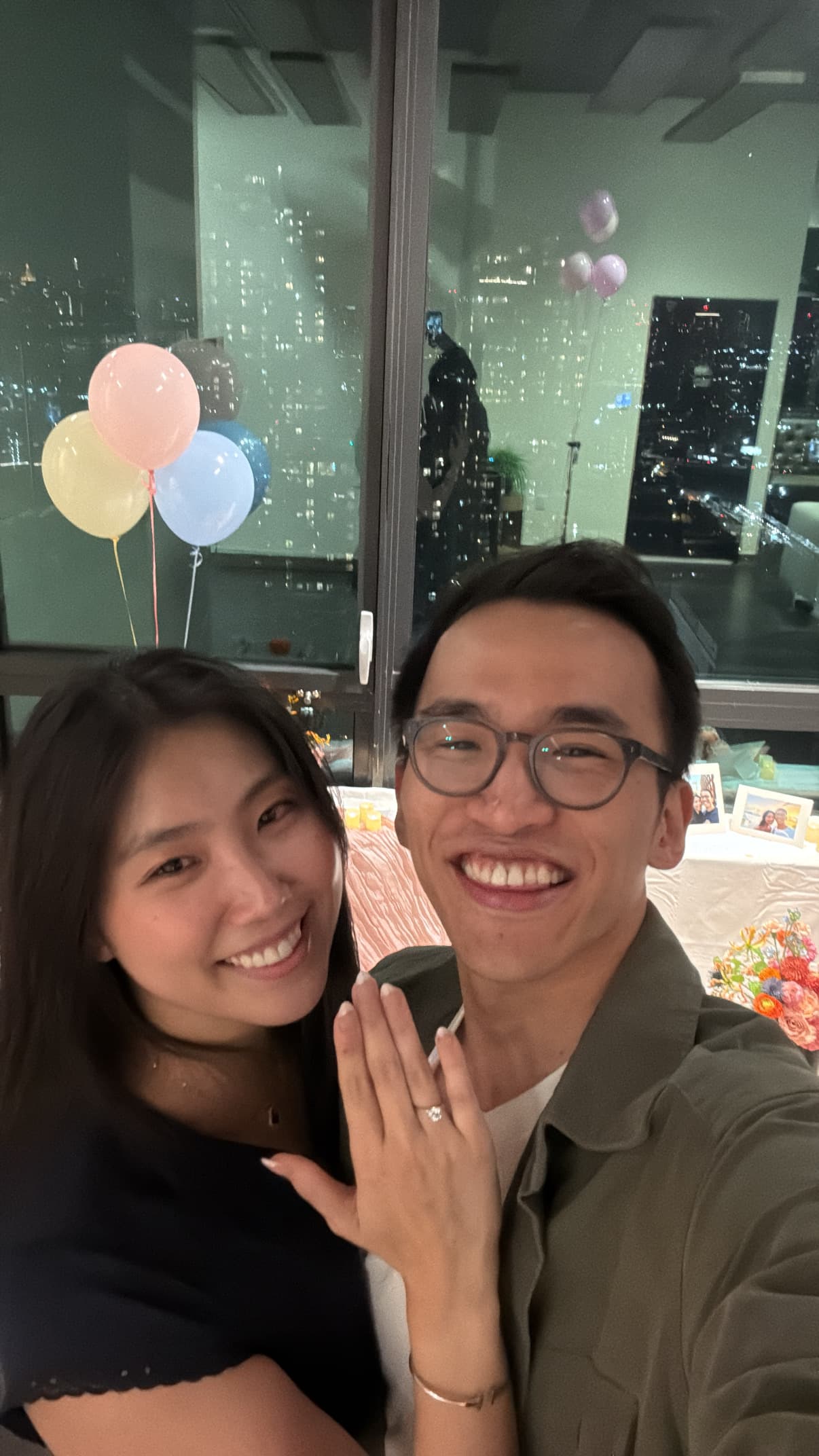 A selfie on the night of the proposal — the ring held up to the camera, balloons and a city skyline behind us.